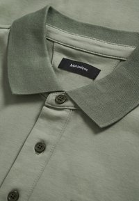 Polo vert kaki en tissu doux, doté d'un col classique, de trois boutons et d'une étiquette en tissu avec l'inscription "Matinique" brodée.