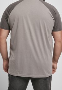 Man i tvåfärgad grå kortärmad t-shirt och mörka jeans, sett bakifrån, med en tatuering på sin vänstra handled.