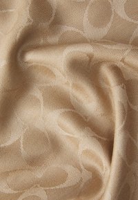 Beige teksturert stoff med en jevn overflate, med et sammenflettet mønster av sirkler i en litt mørkere nyanse.