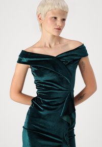 Robe en velours teal avec un design décolleté. Présente un corsage drapé, des fronces à l'avant et un accent en couches à la taille.