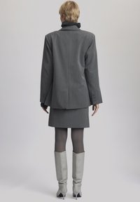 Sivi blazer in krilo s črtami, z teksturiranim črnim ovratnikom. Sive usnjene čevlje do kolen dopolnjujejo obleko.