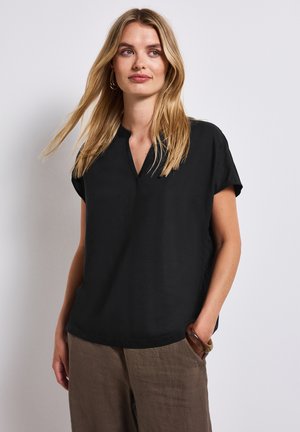 Haut noir à manches courtes avec un décolleté en V. Tissu lisse, coupe décontractée et drapé subtil. Associé à un pantalon en lin beige clair.