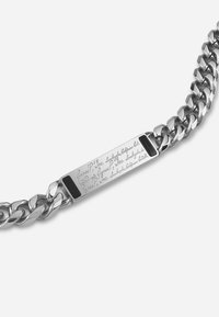 Silver chain bracelet featuring thick links and a rectangular engraved plate with intricate text, accented by small black sections on each end.