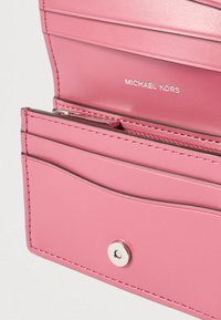 Pink leather wallet featuring multiple card slots, a zippered compartment, and a silver snap closure. "MICHAEL KORS" logo embossed inside.