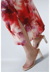 Robe midi fleurie dans des teintes rouge et rose pâle avec une fente sur le côté. Porte des sandales à talons transparents dotées d'une sangle nude et d'un bout ouvert.