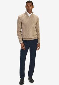 Beige kabelstickad tröja med halvdragkedja, matchad med marinblå byxor och svarta skor. Skjorta med krage under tröjan.