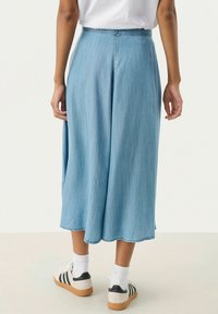 Culotte din denim albastru deschis, cu un design cu picioare largi, margine finisată și o ușoară strălucire. Asortat cu sosete albe și adidași casual.