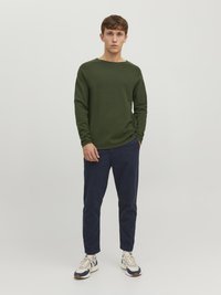 Grønn ribbet langærmet skjorte med båtutringning, kombinert med marineblå slim-fit bukser og hvite joggesko med marineblå og beige detaljer.