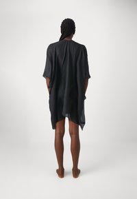 Kaftan in lino nero con vestibilità rilassata, maniche corte e orlo asimmetrico. Texture morbida con una leggera caduta e senza motivi visibili.