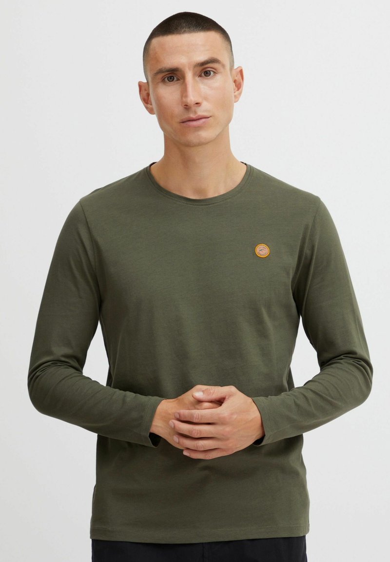 Olive green long-sleeve t-shirt made of soft cotton, featuring a round neckline and a small circular logo patch on the left chest.
