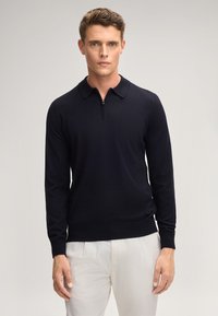 Dunkelblau gestrickter Pullover mit Reißverschlusskragen, langen Ärmeln, gerippten Bündchen und Saum. Der Stoff ist glatt, leicht und weich.