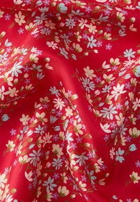 Červená látka s květinovým vzorem zahrnujícím bílé, růžové a modré květy, doplněná zelenými stonky. Hladká textura s lesklým povrchem.