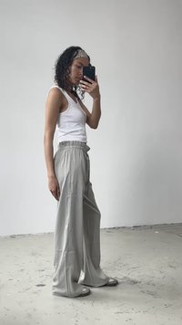 Pantaloni gri evazați cu un brâu elastic, asortați cu un top alb fără mâneci. Materialul pare ușor și neted, având un luciu subtil.