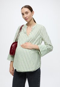 Πουκάμισο με πράσινες και λευκές ρίγες, με κουμπωτό λαιμόκοψη, μανίκια τριών τετάρτων και άνετη γραμμή, σε συνδυασμό με σκούρο τζιν και κόκκινη τσάντα χειρός.