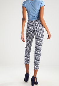 Blå kortärmad topp i kombination med figurnära mönstrade byxor i marinblått och vitt, med ett blommönster och avkortad längd vid vristerna.