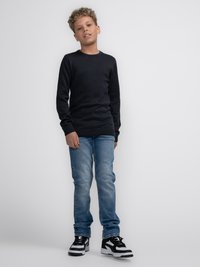 Jersey de punto gris oscuro con mangas largas, combinado con unos vaqueros azul claro y zapatillas en blanco y negro. Diseño sencillo, sin patrones visibles.