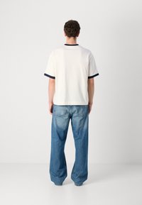 Hvit T-skjorte med marineblå detaljer på ermene, kombinert med løstsittende blå denimjeans, med en falmet vask og baklommer.