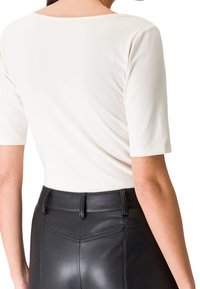 Krémový top s krátkým rukávem a kulatým výstřihem, který je kombinován s černými koženými kalhotami s vysokým pasem, jež mají jemnou texturu a podrobné prošívání.
