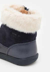 Granatowe bootsy z miękkim, kremowym futerkiem na mankiecie, zamszowa cholewka i gumowa podeszwa z wytłoczonym logo.