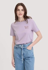 Lila katoenen t-shirt met korte mouwen, met de tekst "tijd om te bloeien" in het rood geborduurd. Draag het met hoog-waist blauwe denim jeans.