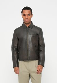 Veste en cuir marron foncé avec un col, fermeture éclair et deux poches latérales. Texture lisse et coupe ajustée.