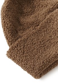 Hnědá texturovaná látka s měkkým, nadýchaným vzhledem a hustým, kudrnatým pleteným vzorem ve složené poloze.