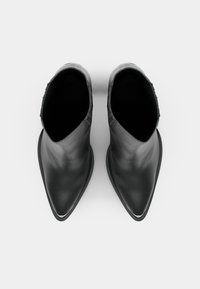 Botas de couro pretas até ao tornozelo com bicos pontudos e textura suave. Apresentam um design de corte baixo e detalhes laterais subtis.