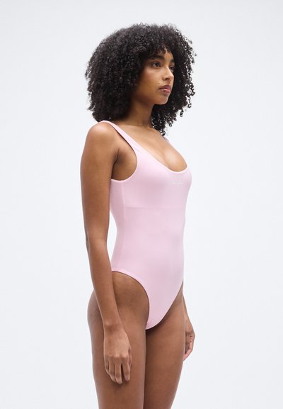 Ροζ ολόσωμο μαγιό με στρογγυλεμένη λαιμόκοψη και φαρδιές τιράντες. Κατασκευασμένο από λείο υλικό, διαθέτει μινιμαλιστικό σχέδιο και μικρό λογότυπο.