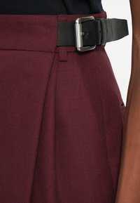 Bordowe spodnie z teksturowanej tkaniny, z czarnym paskiem z srebrną klamrą, z przodu z zaszewkami i bocznymi kieszeniami.