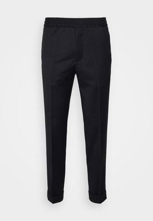 Musta slim fit -mallinen housu, jossa joustava vyötärönauha, edessä laskokset ja käänteiset lahkeet, valkoista taustaa vasten.