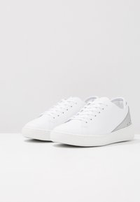 Zapatillas de cuero blanco con textura suave, diseño bajo, puntera redonda y un acento en el talón en contraste gris. Cierre con cordones.