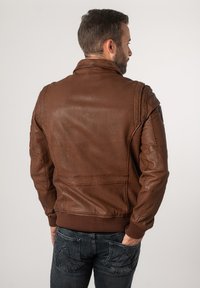 Braune Lederjacke mit geripptem Saum, Schulternähten und Reißverschlusstaschen. Die Rückseite hat eine glatte Textur und minimale Details.