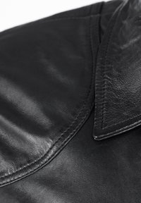 Zwarte leren tas met een gladde textuur, voorzien van een puntige klep sluiting. Zichtbare stiksels langs de randen. Compacte en gestructureerde vorm.