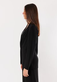 Blazer nero realizzato in tessuto liscio, con vestibilità su misura, rever a destra e maniche lunghe, dotato di chiusura a un bottone e spacco laterale.