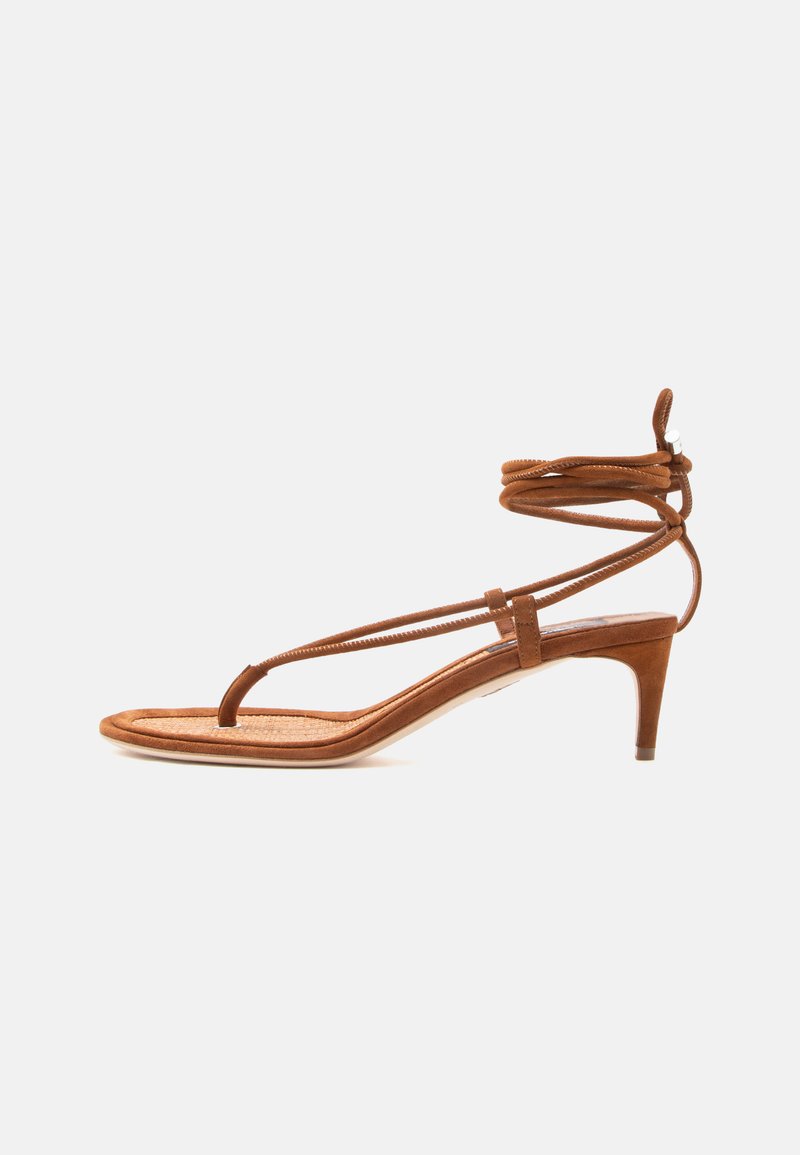 Sandale marron à lanières avec une fine boucle pour l'orteil, des lanières enroulantes autour de la cheville, et un petit talon kitten bas sur fond blanc.