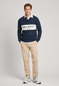 Jūras spēku garo piedurkņu polo krekls ar baltu svītru, uz kura redzams "PEPE JEANS LONDON" logo, savienots ar beisika biksēm un pelēkiem sporta apaviem.