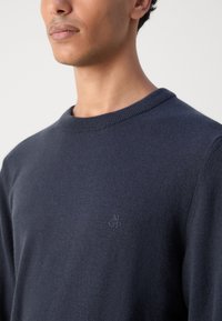 Tengerész navy crew-neck pulóver, puha anyagból készült. Diszkrét logó részlet található a mellrészen. Klasszikus szabás, bordázott nyakkal és mandzsettával.