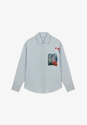 Camicia button-up azzurro chiaro con colletto, caratterizzata da una toppa floreale sulla tasca anteriore e disegni di fiori colorati sulla spalla.