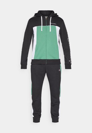 Grüner und schwarzer Trainingsanzug mit einer Reißverschluss-Kapuzenjacke und passenden Hosen. Mit weißen Akzenten und einem Logo auf der Brust und am Bein.