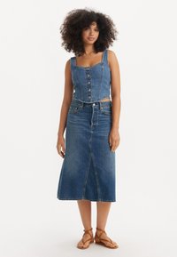 Jeanscropped topp med firkantet utringning og frontknapper, kombinert med et denimskjørt til kneet. Lyseblå vask med synlige sømmer.