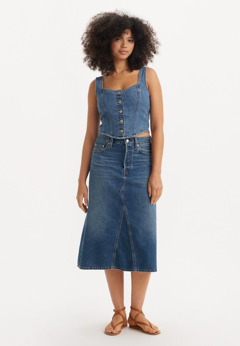Jeanscropped topp med firkantet utringning og frontknapper, kombinert med et denimskjørt til kneet. Lyseblå vask med synlige sømmer.