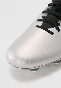 Silver football boot with a smooth, reflective synthetic upper, black laces, and a low-cut design. Features six conical studs for traction.
