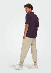 Lilla kortærmet polo shirt med en afslappet pasform, parret med beige sweatpants og hvide sneakers. Glat stof med minimale accenter.