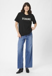 Tricou negru cu "FEMME" scris cu litere argintii, asociat cu blugi albaștri cu talie înaltă și picior larg, împreună cu cizme negre cu toc. Material neted și croi lejer.