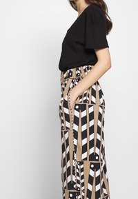 Black cotton T-shirt paired with patterned wide-leg pants in tan, black, and white featuring vertical lines and circular accents.