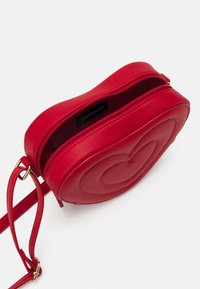 Rød crossbody-taske formet som et hjerte, lavet af glat syntetisk læder, med lynlås og justerbar rem. Detaljer i guldtonet metal.