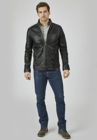 Schwarze Lederjacke mit Reißverschluss vorne, hohem Kragen und zwei vorderen Taschen. Kombiniert mit einem grauen Hemd und blauen Jeans. Glatte Textur.