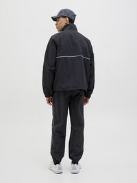 Svart vindjakke med høy krage, med en hvit horisontal stripe. Sammen med matchende svarte bukser og hvite joggesko.