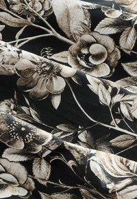 Un tissu noir présentant des motifs floraux complexes en tons de crème et de marron, avec des feuilles et des fleurs détaillées, mettant en avant texture et profondeur.