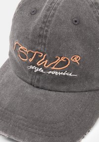 Grå bomullscap med broderad orange och vit text, med en strukturerad skärm och sömdetaljer på kanten.